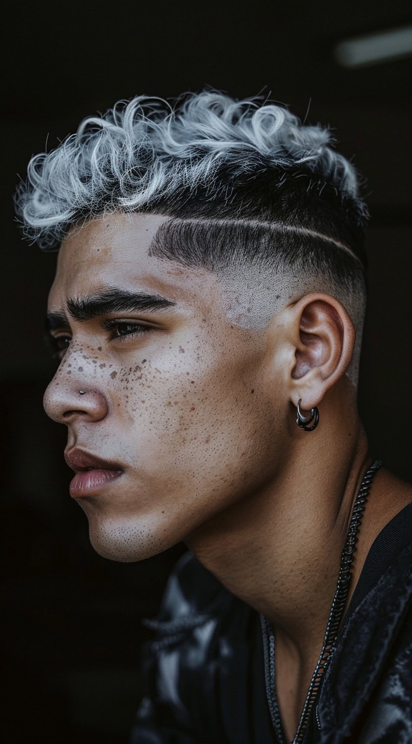 In this photo, a man with a black undercut and a short white wavy top is gazing to the side.