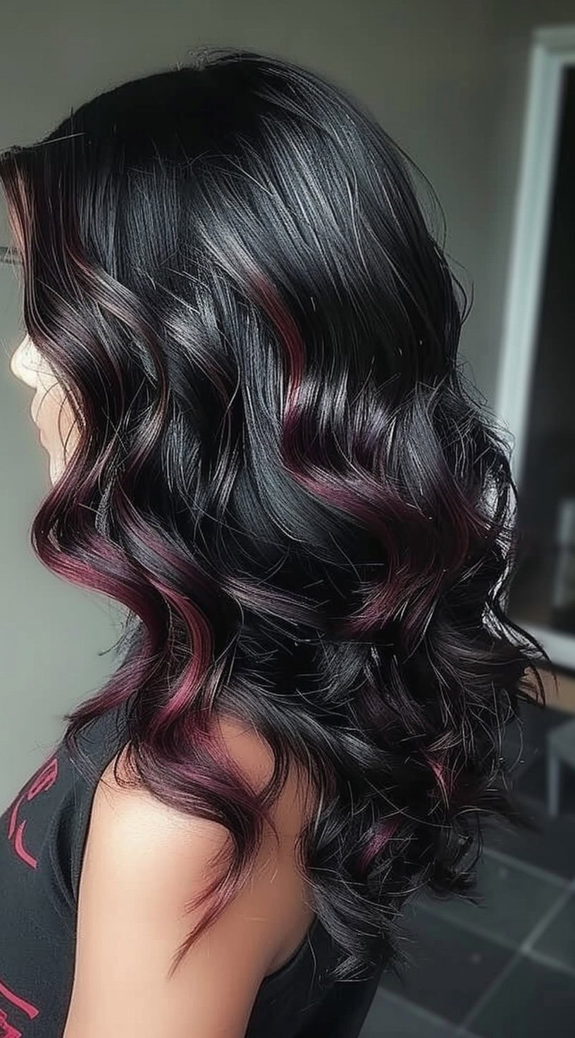 In this photo, a person with wavy black hair has subtle burgundy highlights peeking through the layers.