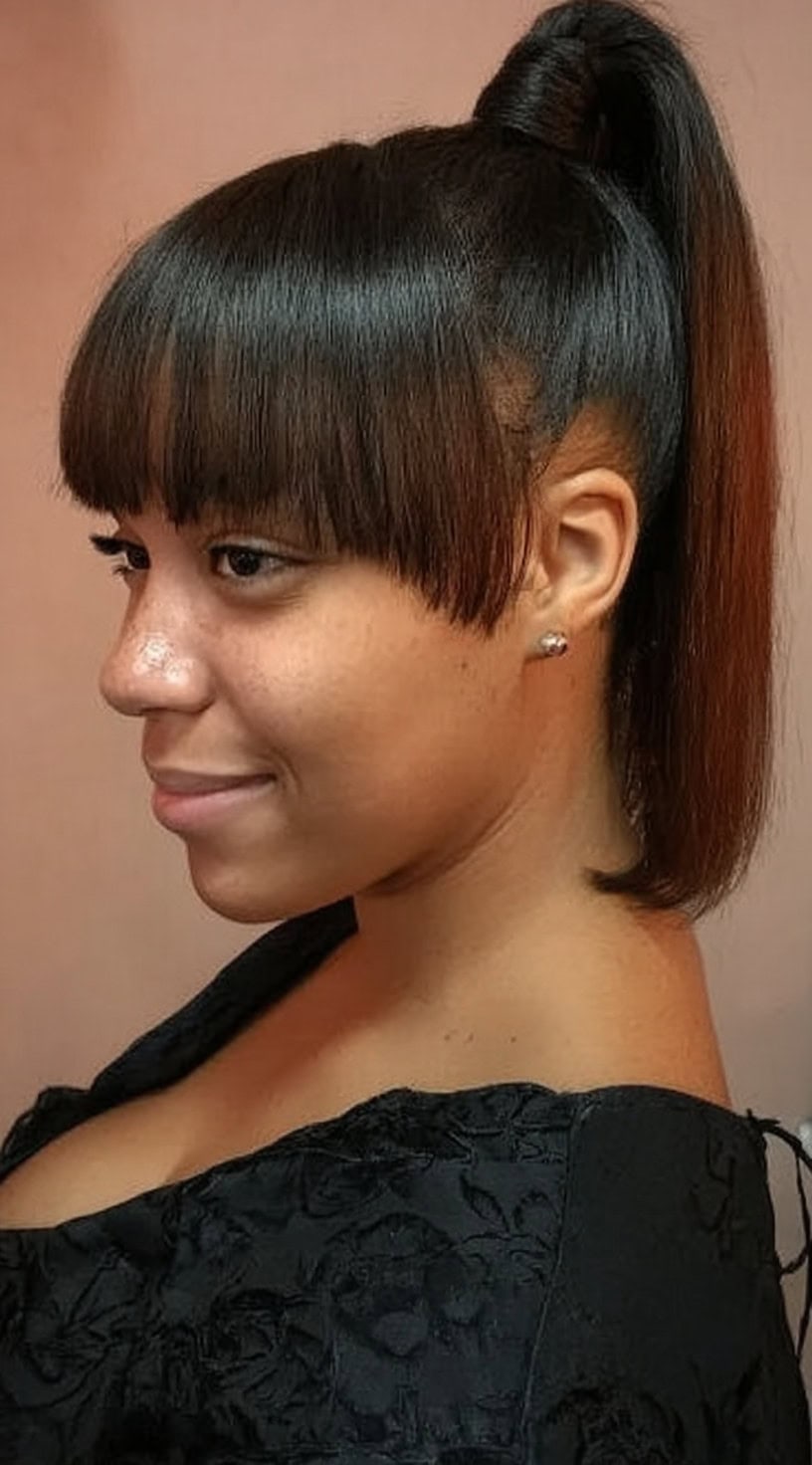 Side view of a woman with a polished mid-high ponytail and blunt straight-across bangs.