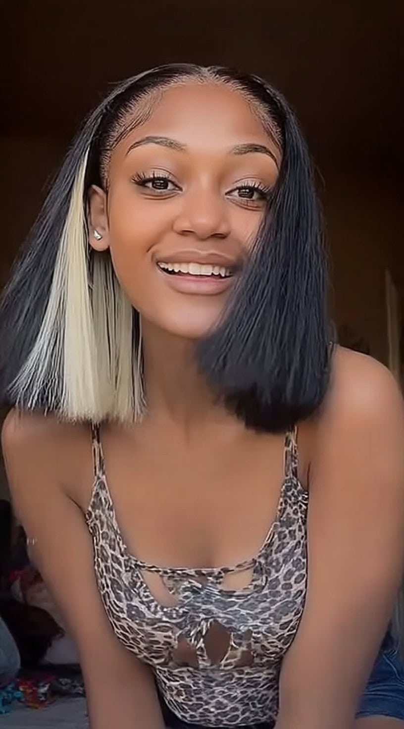 Young woman with a blunt bob featuring bold black hair and wide platinum peekaboo sections near the face.
