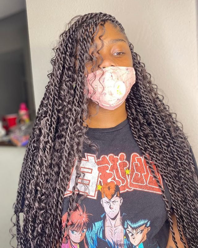 Person wearing a pink mask and a black T-shirt with long, flowing Boho Knotless Senegalese Twists.