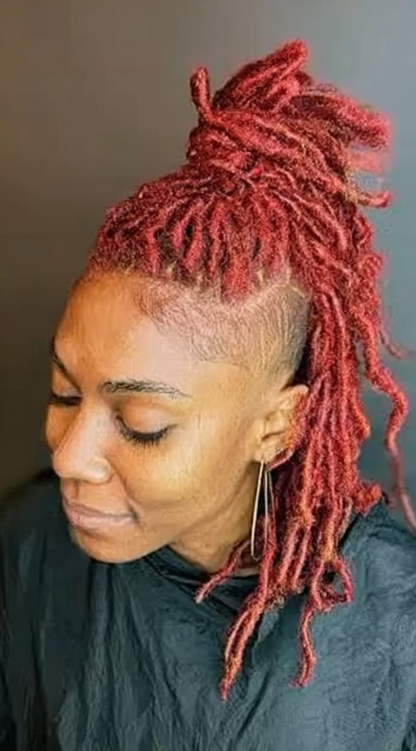 Side view of bright red locs styled into a half-up mohawk with shaved sides.