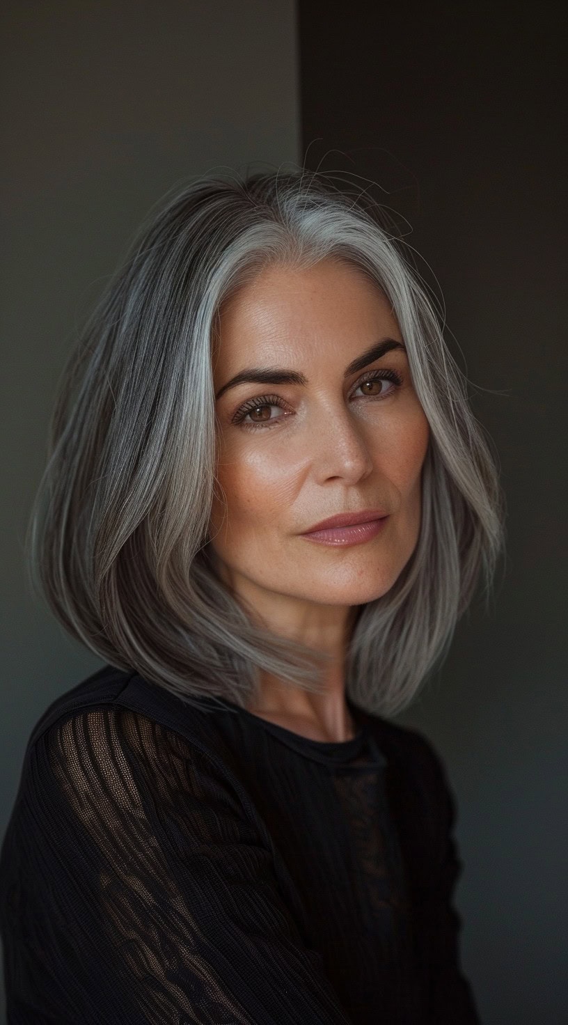 In this photo, a woman with a classic bob featuring silver streaks is shown against a simple background.