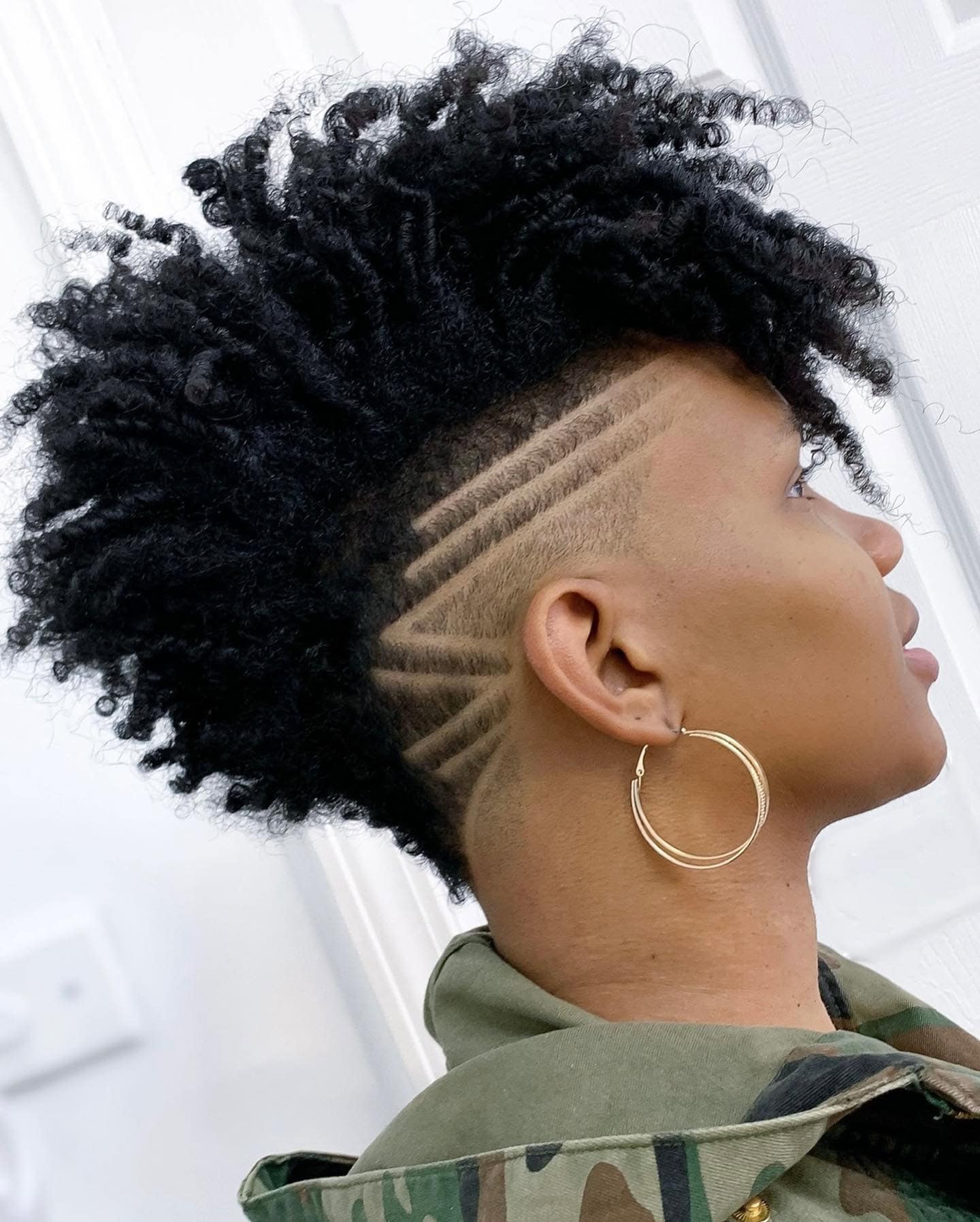 Curly mohawk with intricate shaved side patterns.