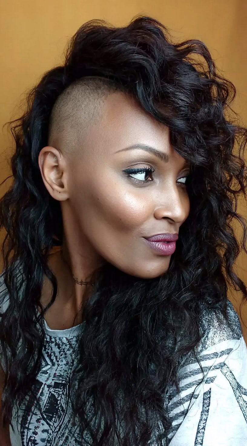 Black woman with long defined curls swept to one side, revealing a clean undercut on the opposite side.