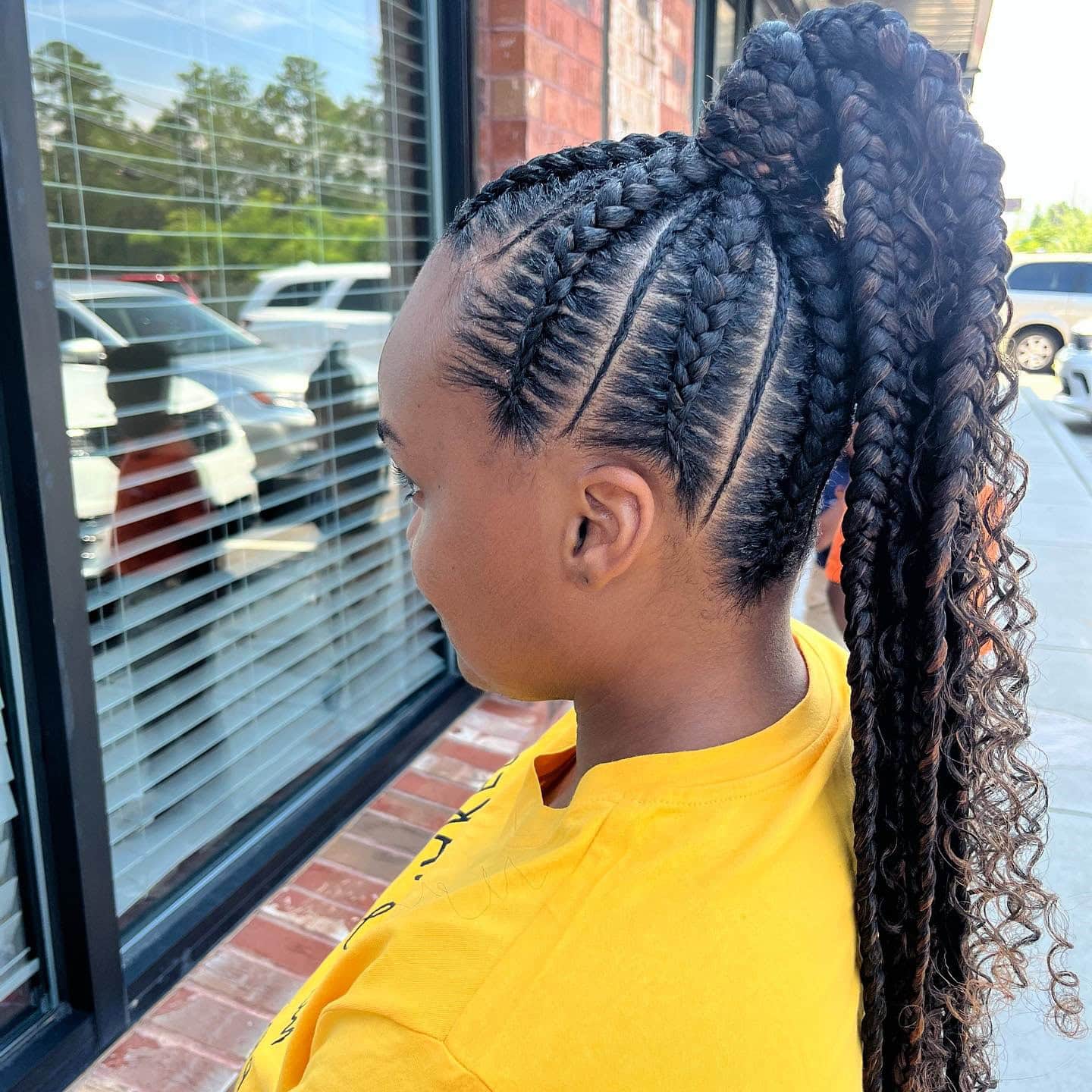 Side view of a person with a high braided ponytail, showing neatly braided cornrows leading to a voluminous ponytail.