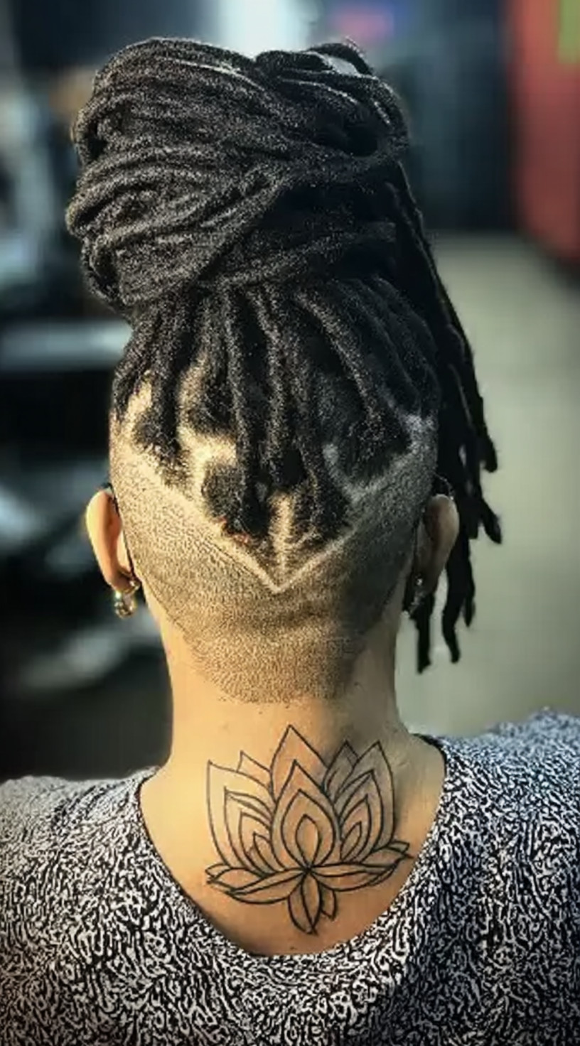 Rear view of a woman with a high loc bun and a heart-shaped shaved design at the back of the head.