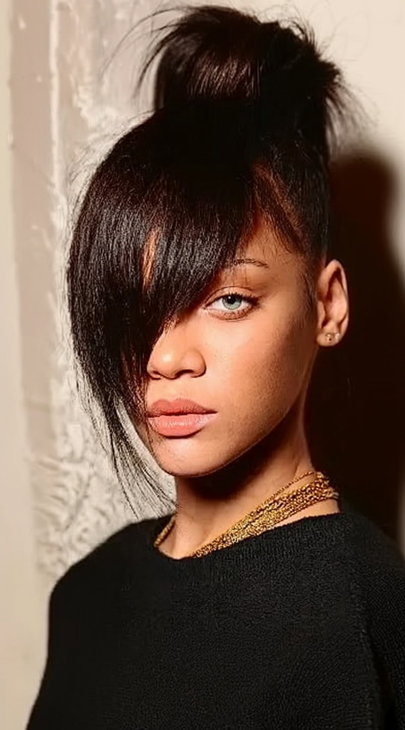 Young woman with a high bun and long asymmetrical bangs covering one eye.