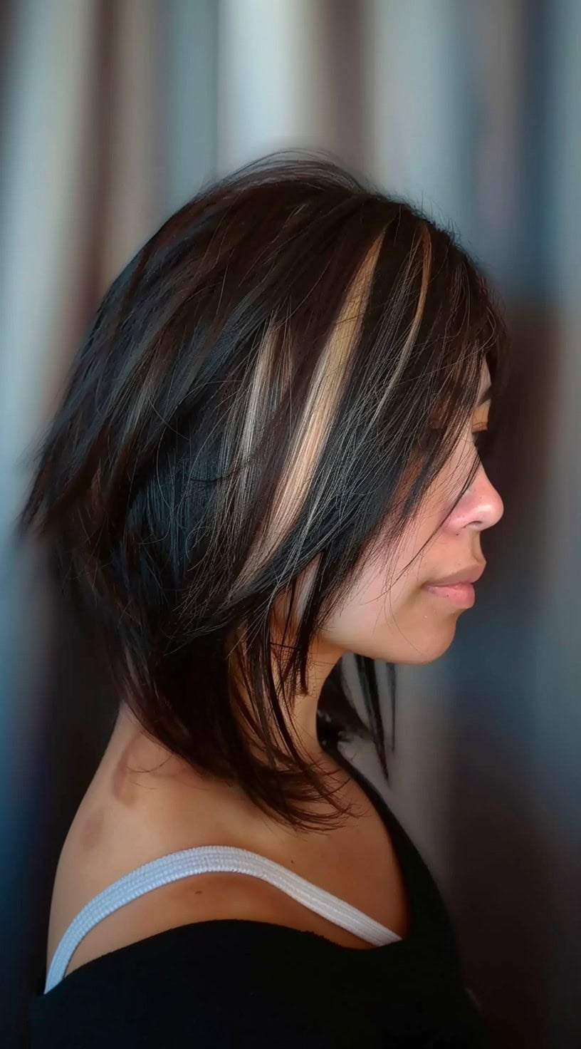 A woman with a layered bob haircut has blonde highlights mixed into her dark hair, adding dimension.