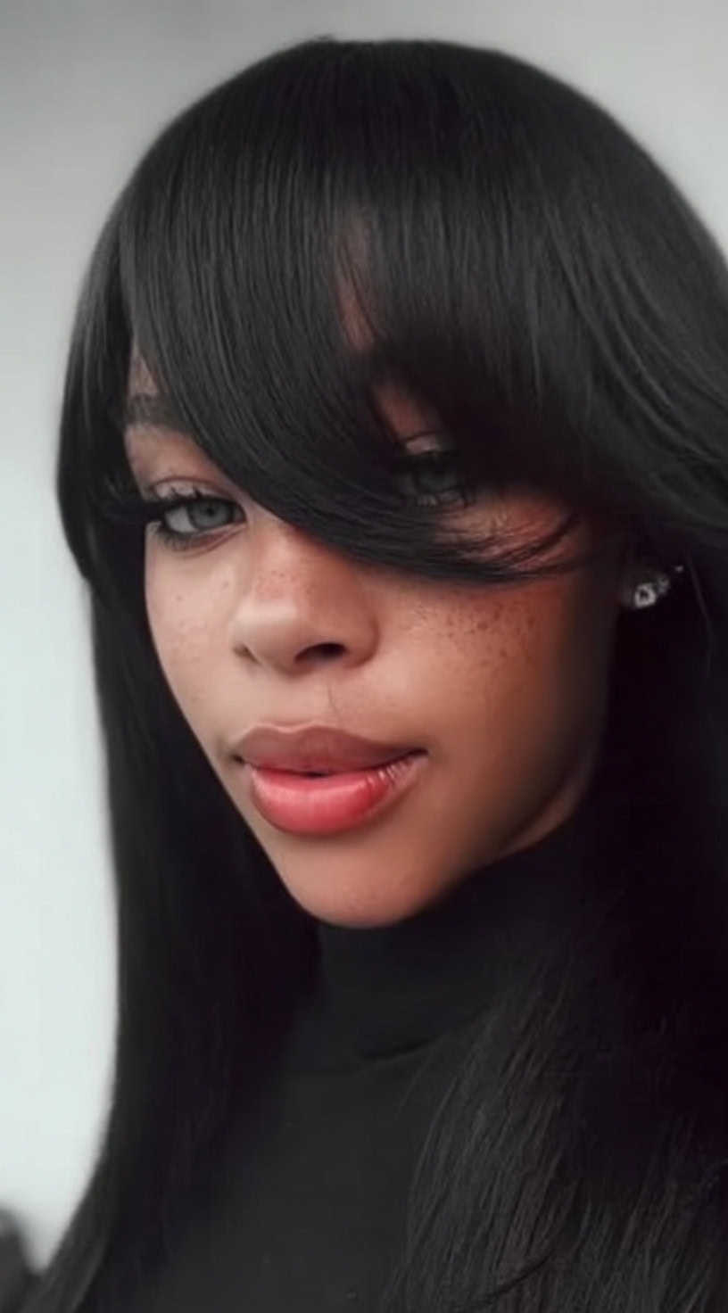 Young woman with long straight hair and thick side-swept bangs covering one eye.