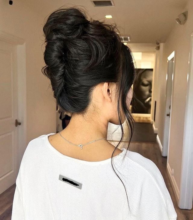 A woman with dark hair styled into a modern French twist updo, with loose strands framing her face.