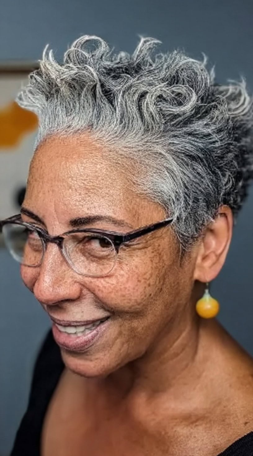 Close-up of a woman with naturally curly salt and pepper hair styled into a voluminous cropped pixie.