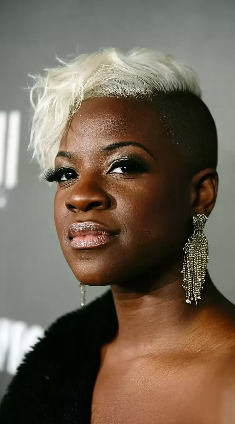 Black woman with a platinum textured fringe and a completely shaved side at an event.
