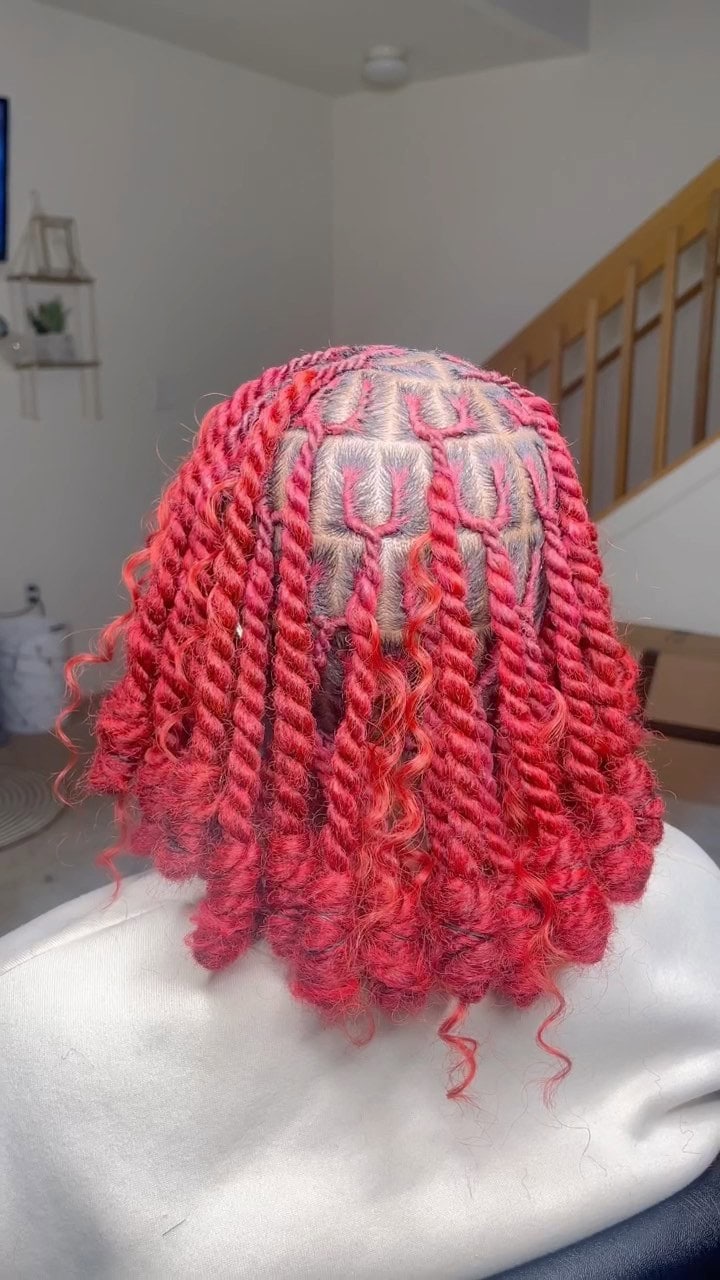 Invisible locs dyed red and styled with defined curls for a vibrant look.