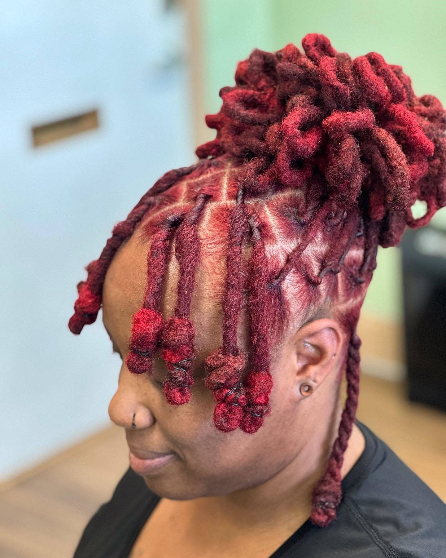 Short red invisible locs styled in an updo with curled ends for a unique and striking look.