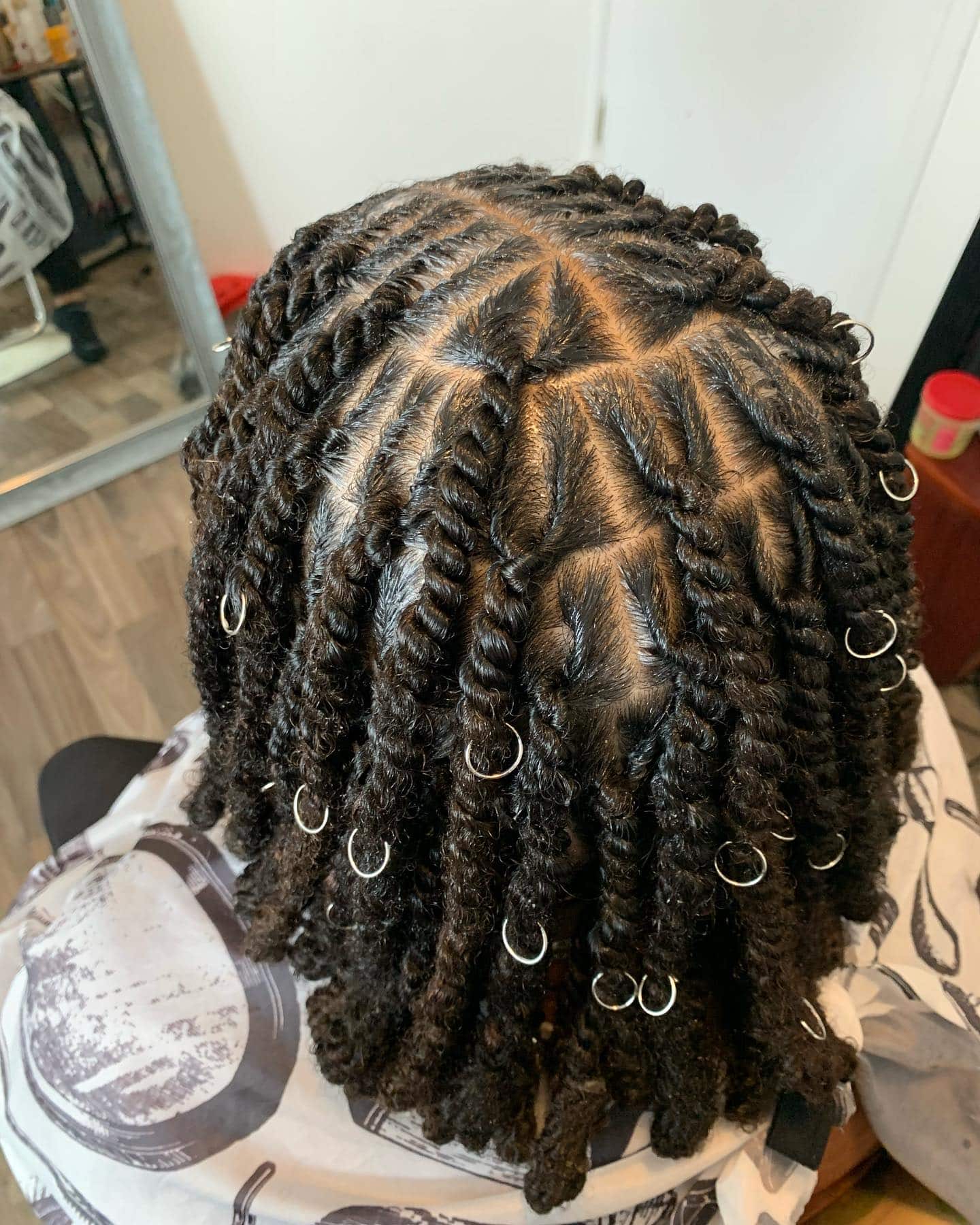 Close-up view of short invisible locs arranged with clean triangle-shaped parting and small silver hair cuffs.