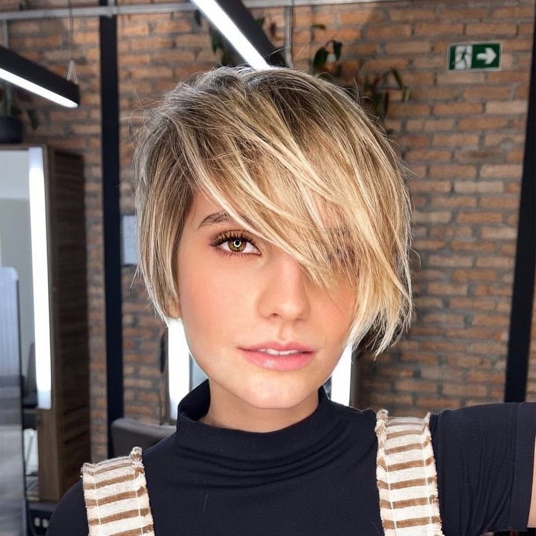 This photo shows a woman with a short textured pixie cut and bangs covering one eye.