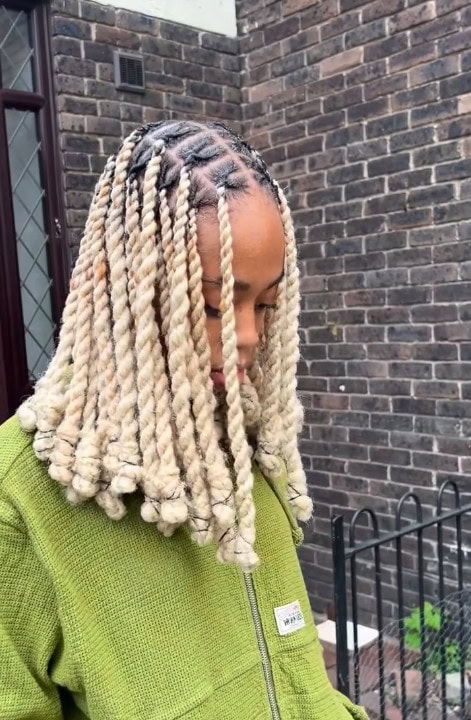 Blonde shoulder-length invisible locs with uniform twists and curled ends framing the face.