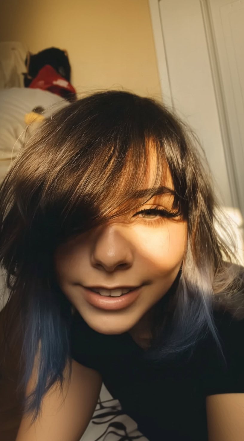 Young woman with shoulder-length shaggy hair and wispy bangs covering one eye.