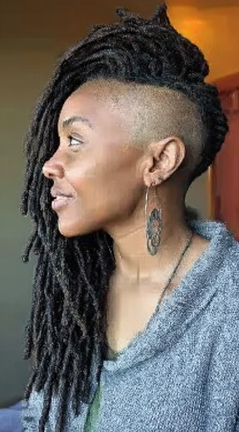 Side view of a woman with long locs swept to one side in a mohawk style with shaved sides.