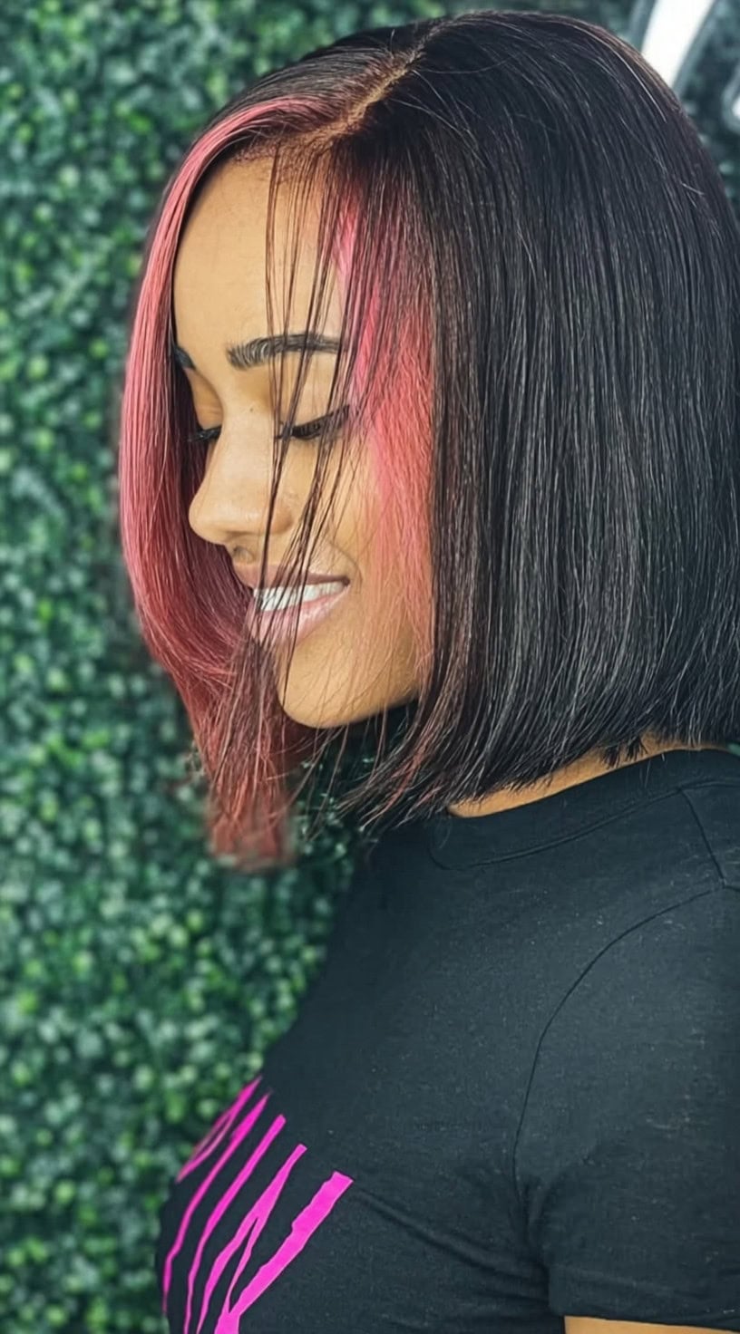 Side view of a woman with a sleek dark bob featuring bright pink peekaboo highlights near the front.