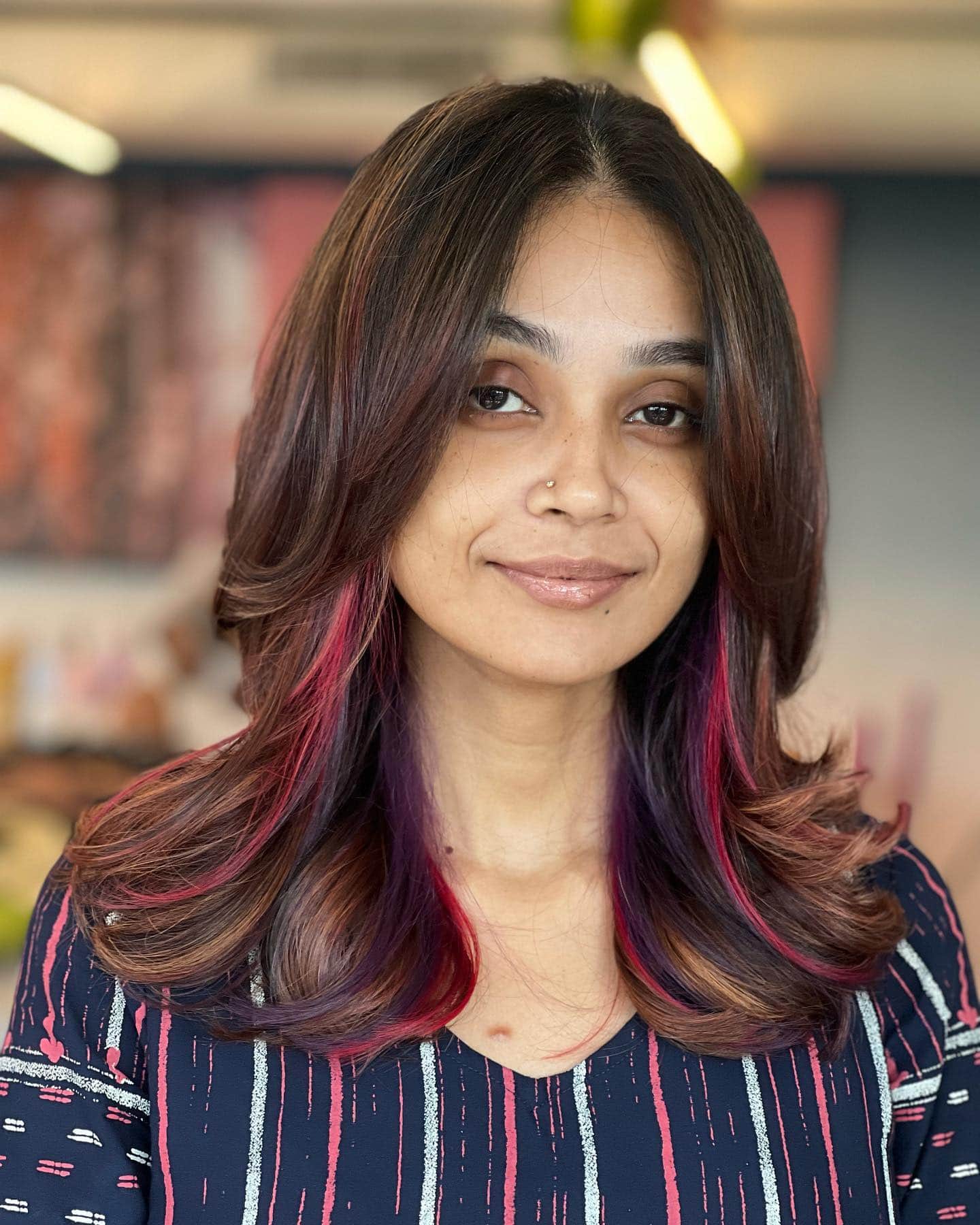 A woman with dark, layered hair featuring subtle burgundy and purple highlights peeking through.