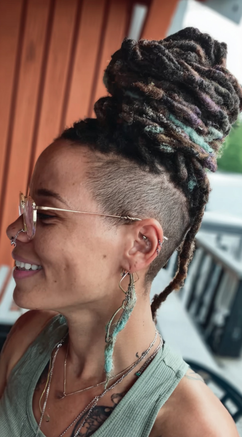 Side view of a woman with a tall loc bun wrapped high on the head, featuring pastel accents and a shaved undercut.