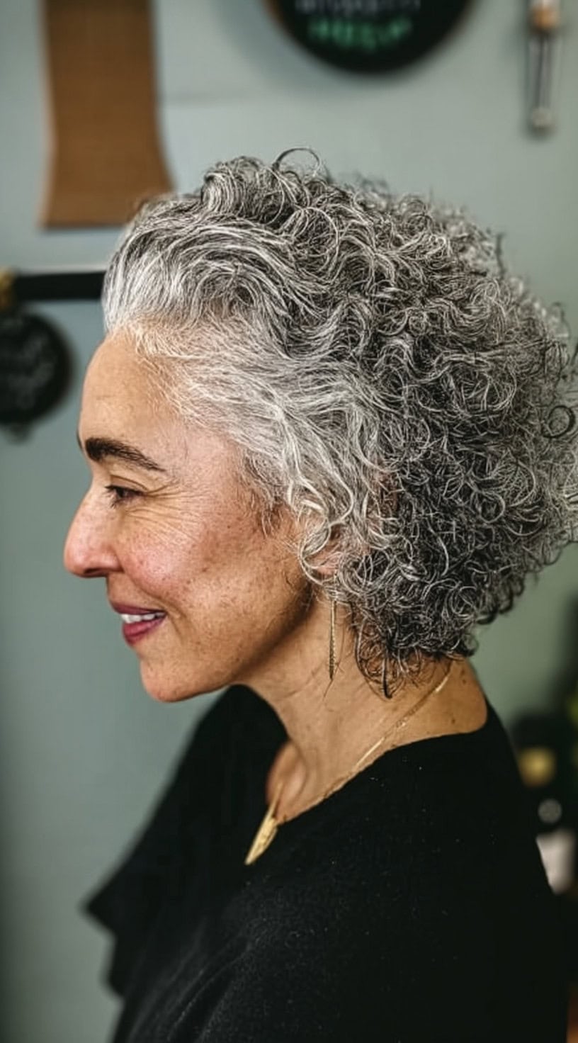Side view of a woman with a rounded crop of tight curls in a salt and pepper color blend.