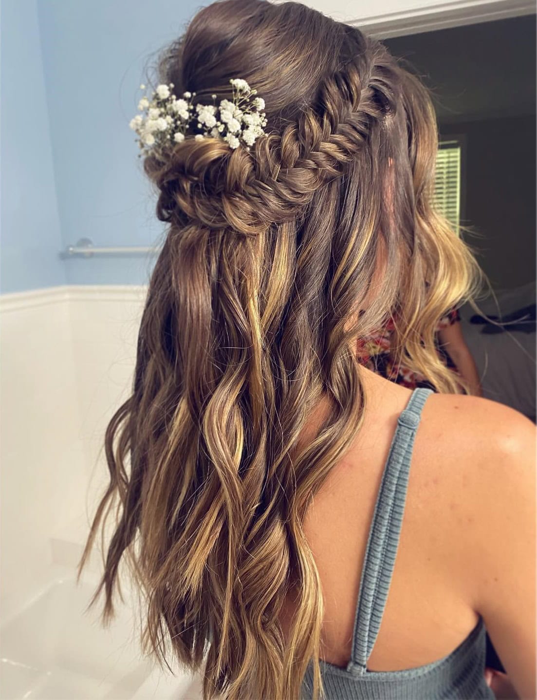 This photo shows a half-up, half-down hairstyle with a fishtail braid crown adorned with white flowers.