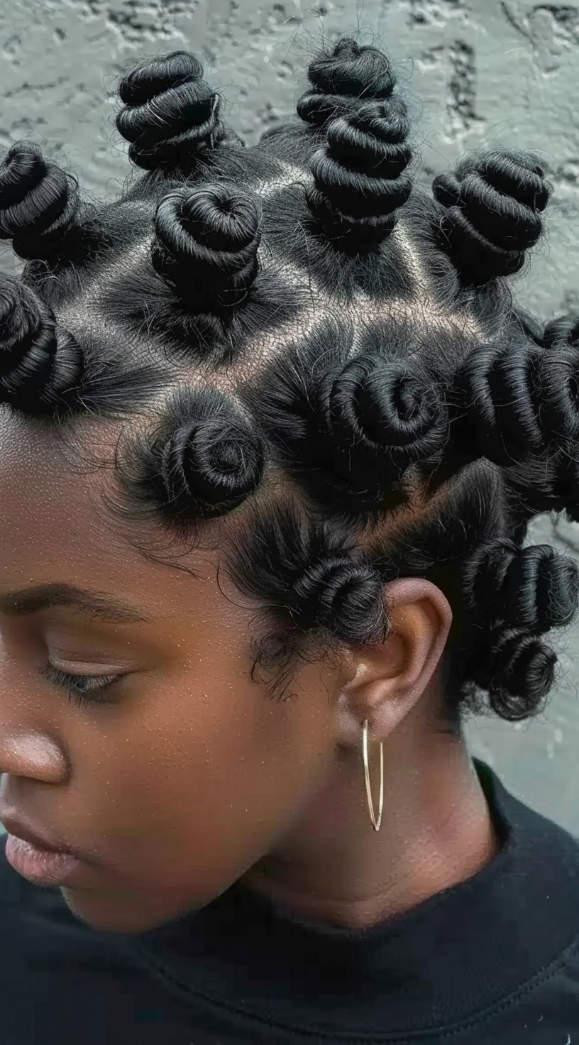 Tightly coiled bantu knots on a young woman's head with gold hoop earrings.