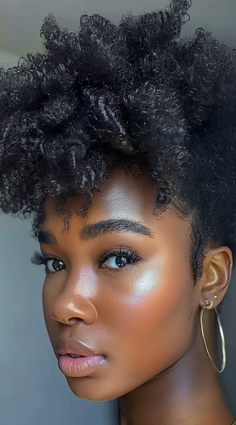 A woman with 4c hair styled in a curly pineapple updo.