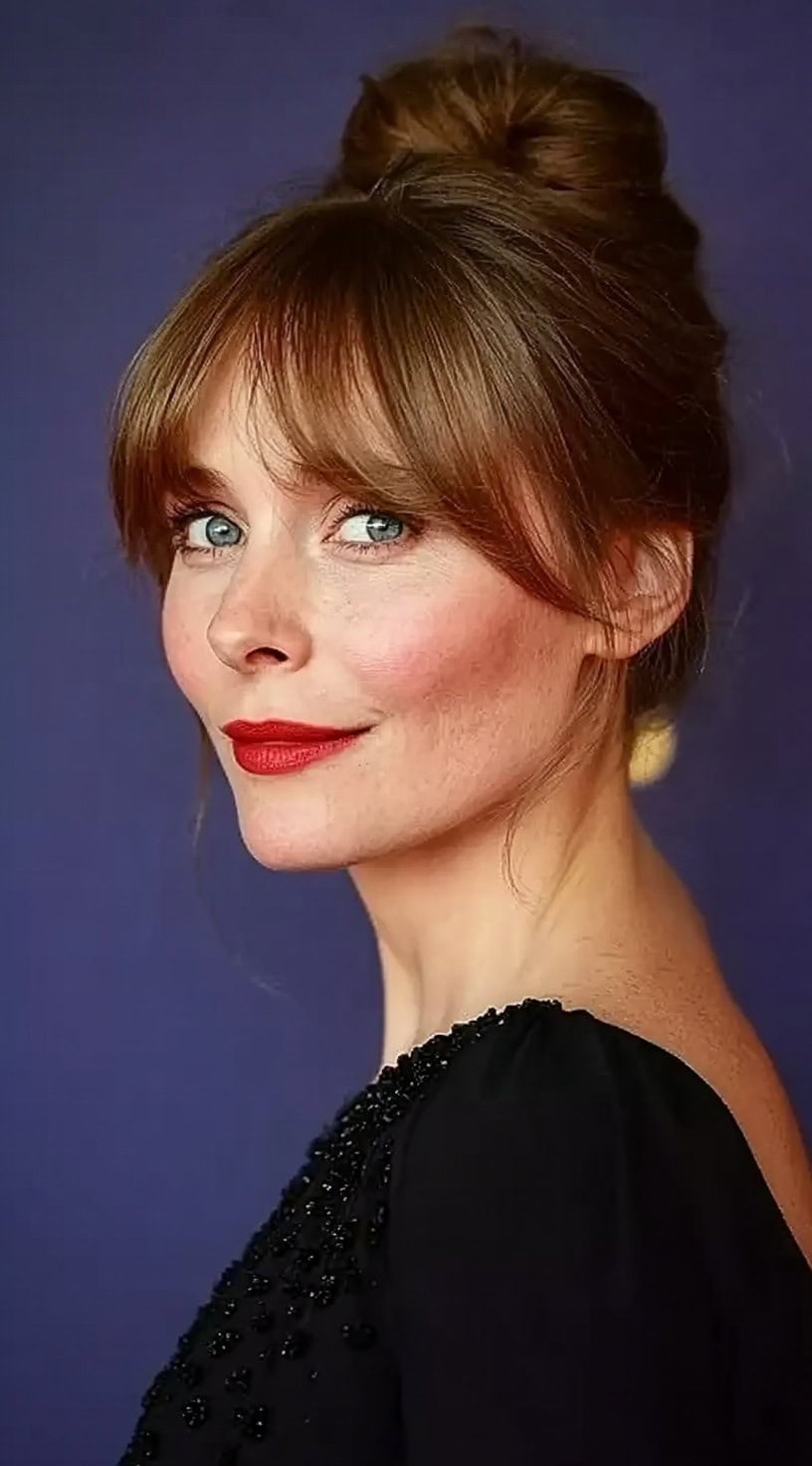 A woman wearing an elegant updo with soft bottleneck bangs and loose strands framing her face.