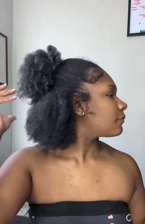 A side-profile image of a woman wearing a half-up puff with textured 4c hair left loose at the back.