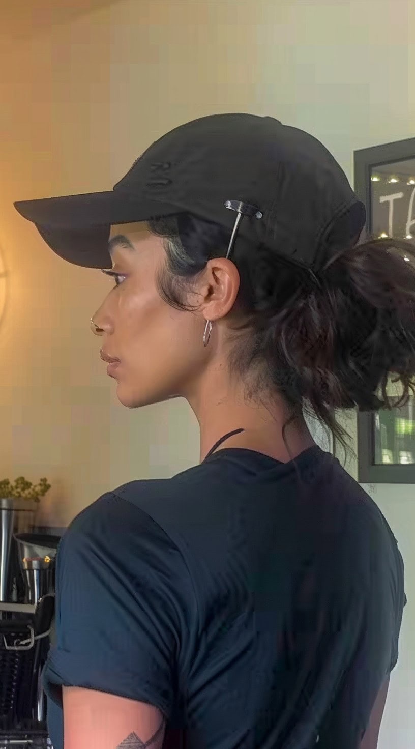 Side view of a woman with a low bun wearing a black cap in a casual setting.