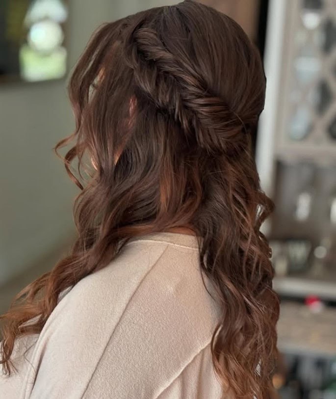 Back view of long brown hair styled in a half-up fishtail braid with soft, loose waves flowing down the back.