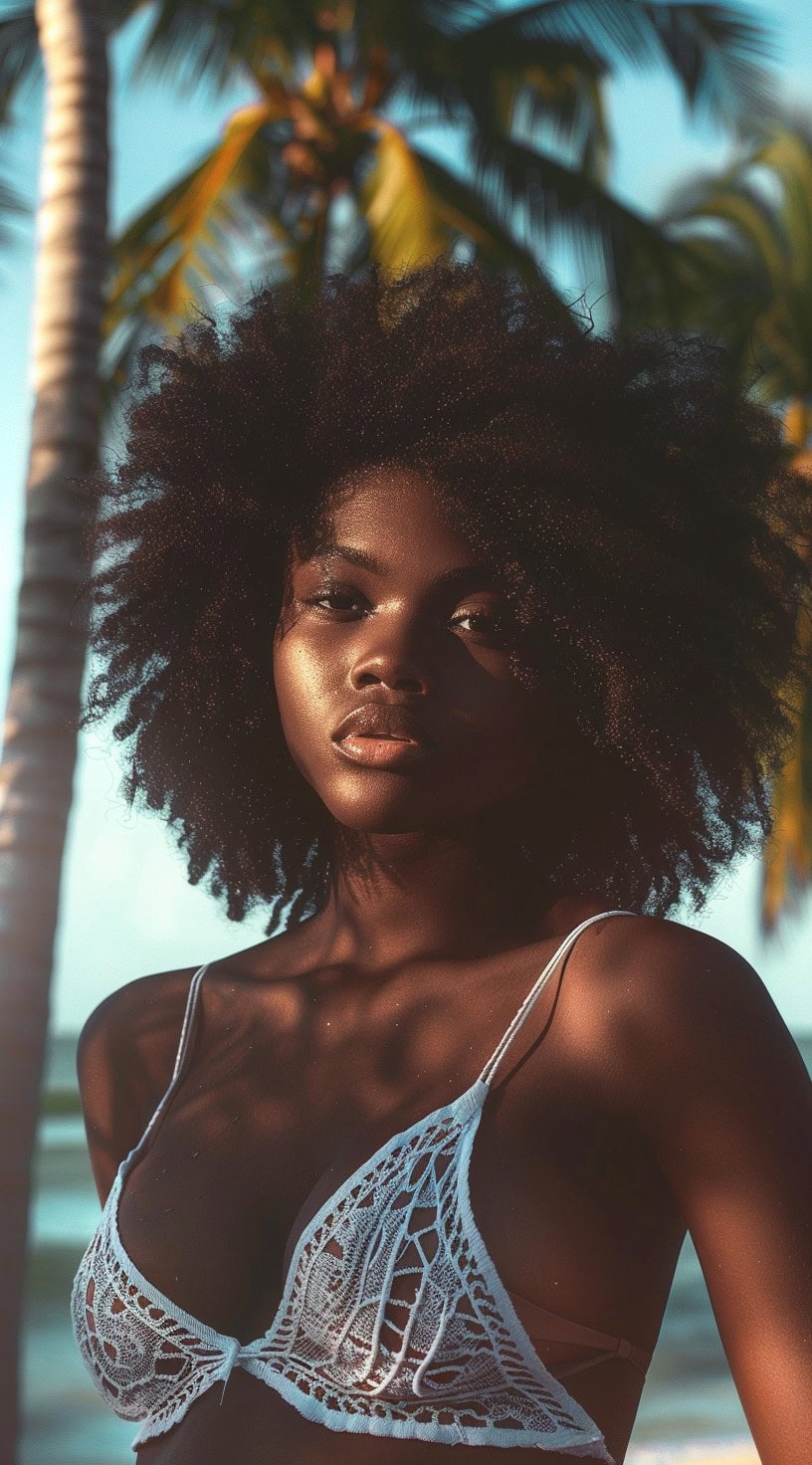 A woman with a textured afro and subtle highlights is standing by palm trees, wearing a stylish crochet top.