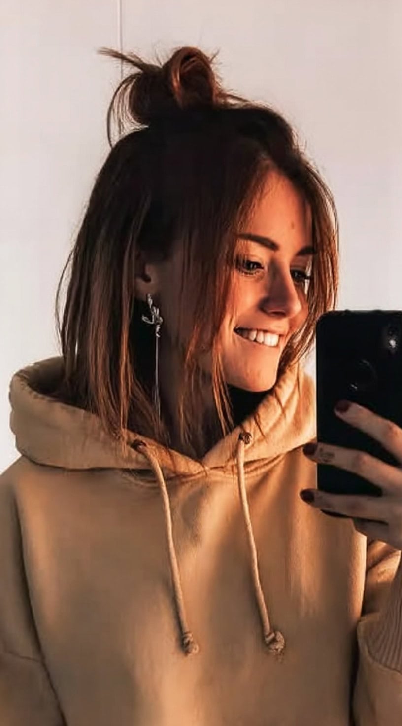 A young woman with straight shoulder-length hair in a hoodie wearing a messy half-up bun with face-framing pieces.