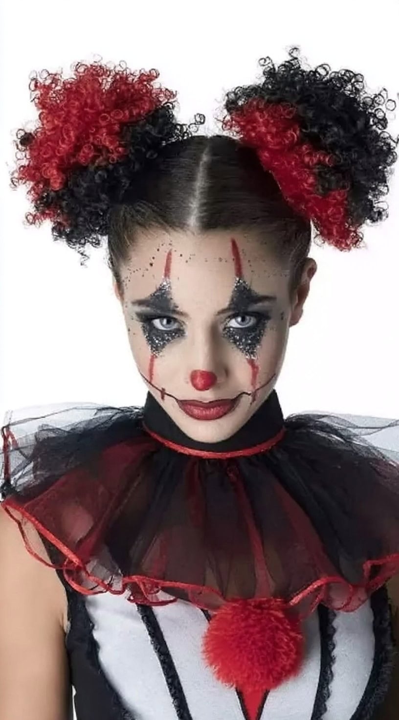 Person with two puffy afro buns dyed red and black, paired with glittery black clown eye makeup on a white background.