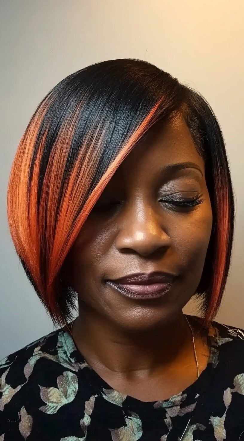A woman with an angled bob featuring sleek black roots transitioning into vibrant orange highlights.