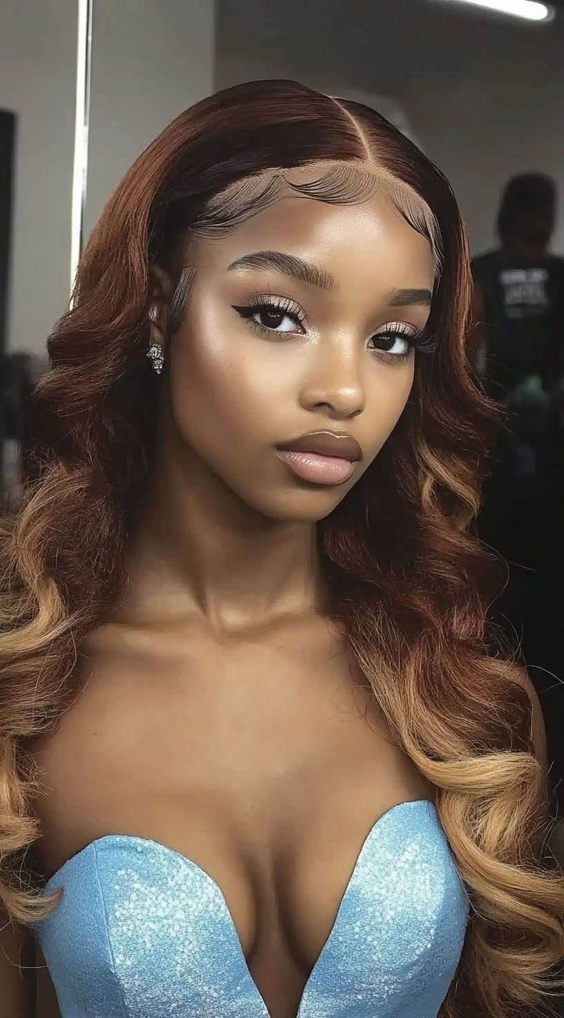 A woman with chestnut brown ombré waves, styled in a middle part with sleek edges, blending seamlessly into soft curls.