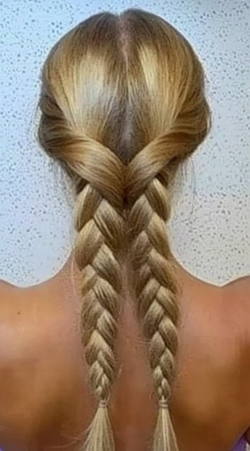 A woman with golden blonde hair styled into two symmetrical Dutch braids that meet at the nape of her neck.