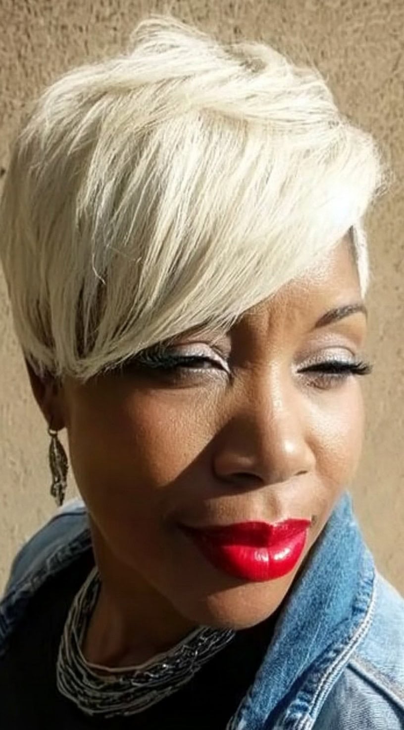 A woman with a platinum blonde pixie cut featuring side-swept bangs and textured layers.