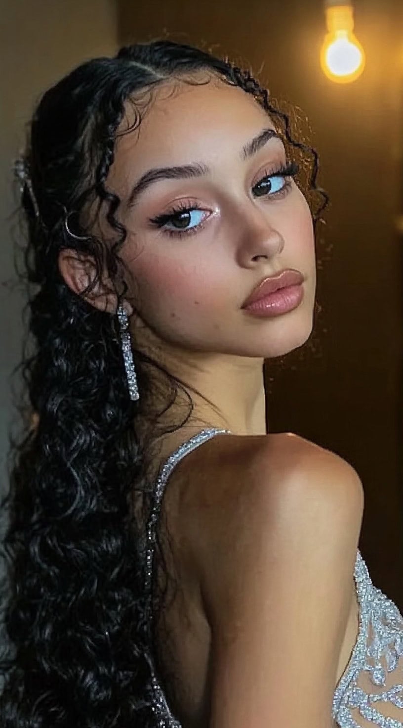 A woman with long, wet-look curls cascading down her back, with delicate face-framing tendrils, wearing a sparkling gown and long crystal earrings.