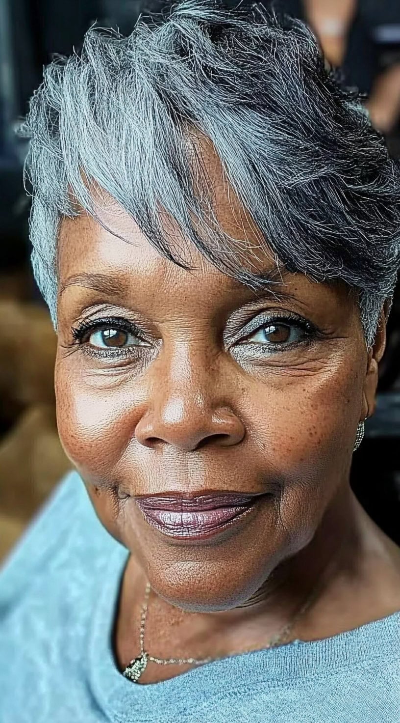 A graceful older Black woman with a silver feathered pixie cut, featuring wispy layers that frame her face beautifully.