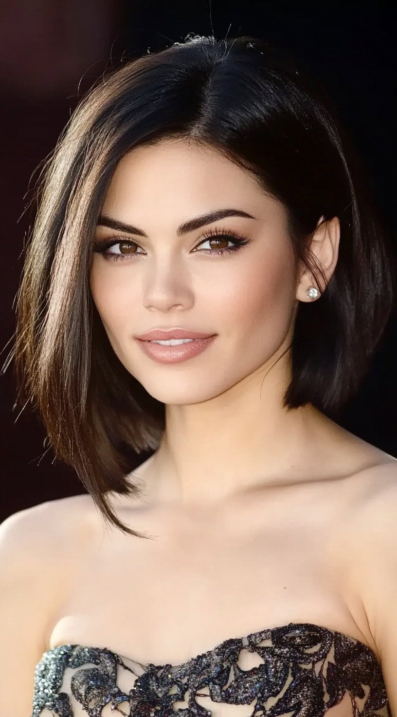 A woman in a strapless black lace dress with a sleek, chin-length angled bob, tucked slightly behind one ear.