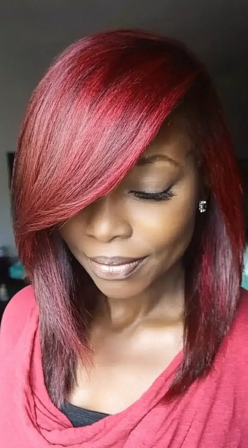 A woman with a sleek, shoulder-length lob dyed in deep burgundy with a long side bang covering one eye.