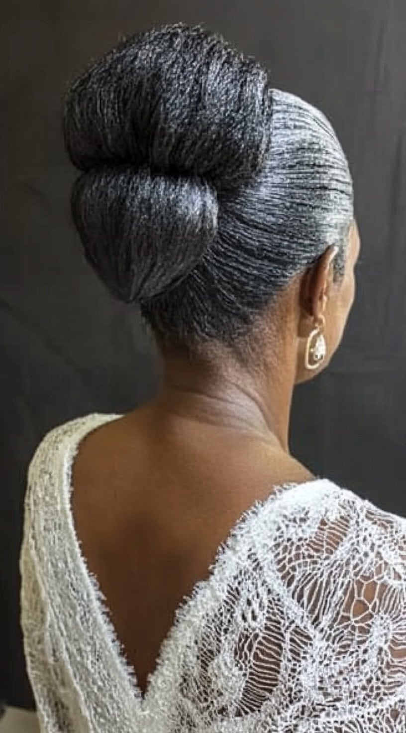 Rear view of a mature woman with sleek gray hair styled into two stacked, rounded buns at the back of the head.