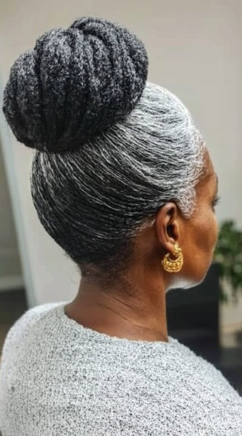 Rear-side view of a woman with sleek silver hair neatly styled into a large, twisted bun.