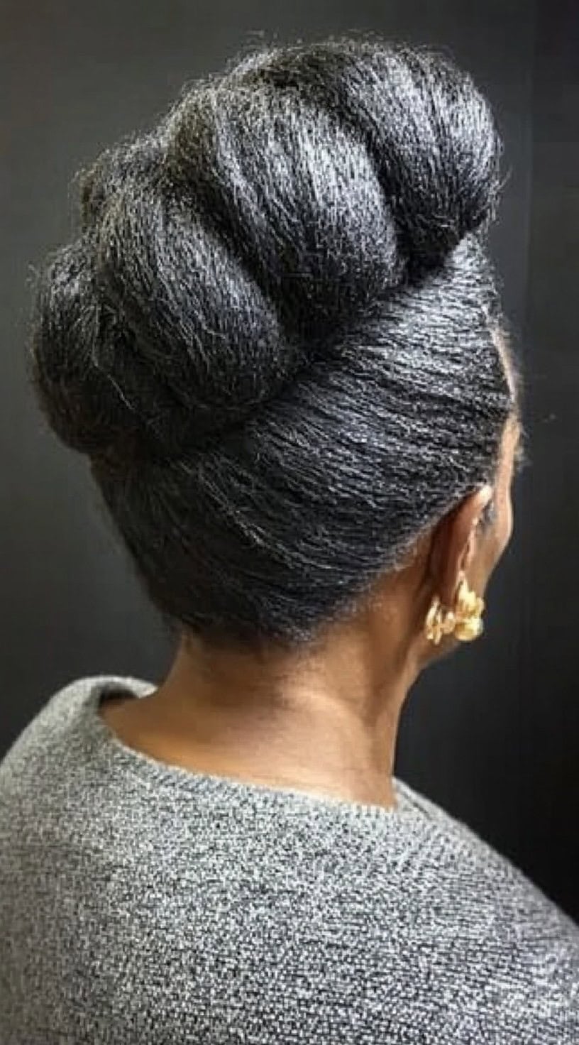 Back view of a woman wearing an elegant, neatly rolled pompadour hairstyle, emphasizing sleek texture and volume.