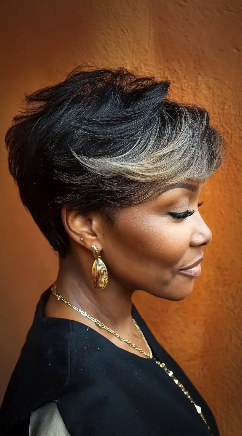 A woman with a short, textured pixie cut featuring soft caramel highlights for added dimension.